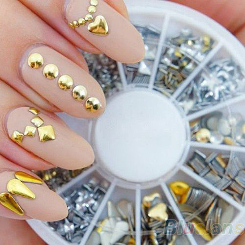 DIY decorative nail art stickers with gold acrylic embellishments on matte nude nails and assorted silver and gold nail decorations in a round storage container